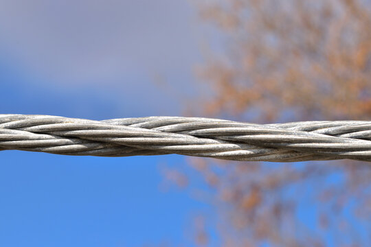 Twisted steel cable with cloudy sky background.