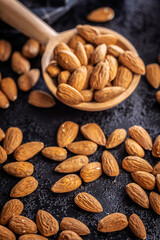 Almond kernel nuts on wooden spoon on black table.