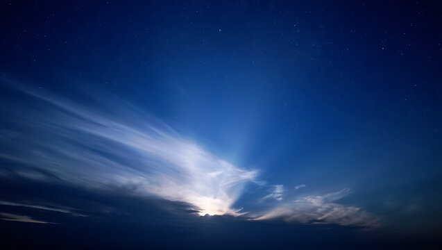 Dramatic celestial display of sunrays breaking through dark clouds against a deep blue sky with stars, creating a breathtaking and ethereal atmospheric phenomenon
