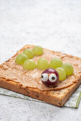 Creative snack idea with peanut butter and grapes shaped like a caterpillar on toasted bread