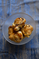 Mini chocolate croissants in transparent bowl on blue background, golden flaky pastries with rich chocolate filling, delicious dessert
