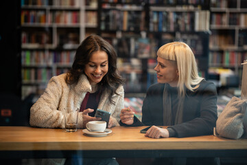 Women friends talking and smiling in library cafe