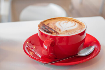 Cup of latte sprinkled with cinnamon in a red cup on a light background