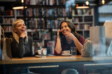 Women friends laughing enjoying coffee and talking on phone