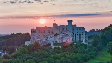 Aerial photograph showing the medieval castle ruins in Ogrodzieniec, Poland during sunrise, surrounded by dense forest and warm morning light