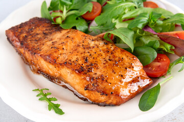 Grilled salmon fillet with fresh green salad and cherry tomatoes on a white plate. Keto diet.