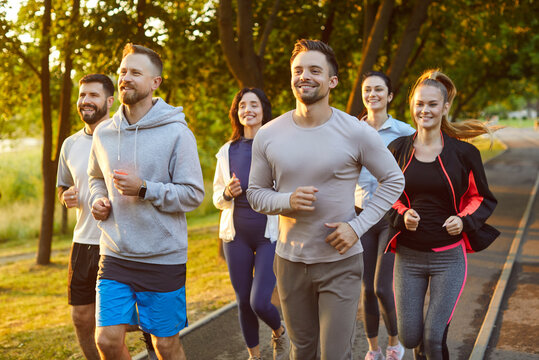 Group of runners jogging in park at morning. Healthy marathon of athletes in sportswear and sneakers running along path, team enjoying summer fresh air and outdoor cardio sport exercises in teamwork