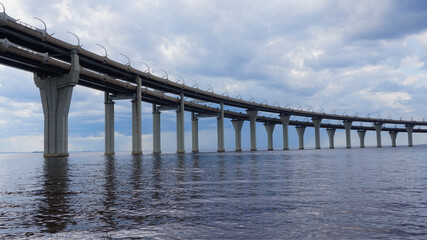 Fototapeta premium Modern elevated bridge stretching across the water with massive concrete supports under a cloudy sky. Architectural infrastructure shot suitable for themes of engineering, transportation, construction