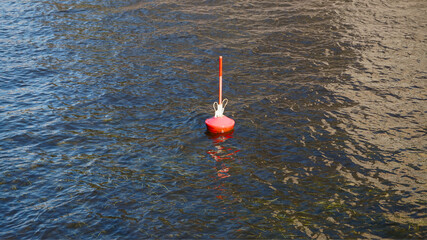 Red navigation buoy floating on rippling blue water. Marine safety marker suitable for themes of navigation, seascape, boating, and maritime environment.