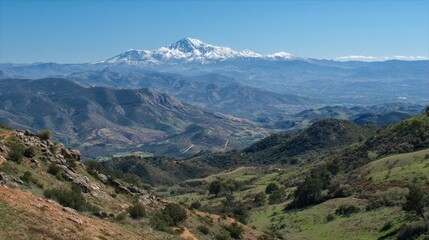 Fototapeta premium Snow covered peaks rise majestically over vibrant green valleys on a sunny day in the mountains.