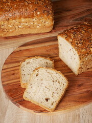 Two loaves of seeded bread on wooden cutting boards, with one partially sliced to reveal the interior. Two slices of the bread are also visible.