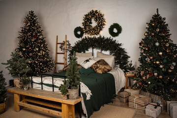 Cozy bedroom decorated with festive green fir trees, garlands, pillows and a Christmas tree
