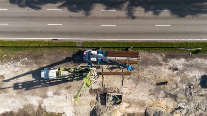 Aerial view of road construction repair site with heavy machinery, workers, next to moving car traffic on a sunny day