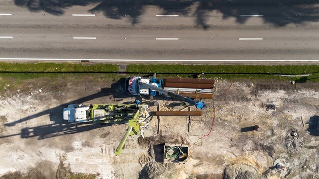 Aerial view of road construction repair site with heavy machinery, workers, next to moving car traffic on a sunny day - Powered by Adobe