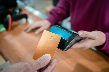 A hand holds a gold bank card and makes a contactless payment on a card reader held by a shop employee, illustrating modern retail transactions.
