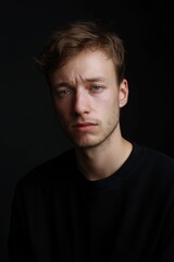 Fototapeta premium Serious caucasian young adult male in black shirt against dark background