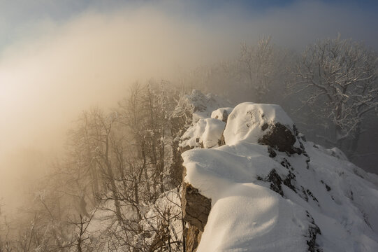 View of snow-laden rocks and frosted trees emerge from a swirling mist, a winter wonderland scene on Vysoka mountain, Vysoka mountain, Kuchyna, Bratislava Region, Slovakia.