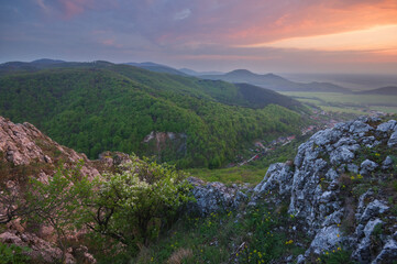 View of verdant hills roll under a painted sky, where the day's last light kisses the horizon, seen from rocky heights, Krslenica, Plavecky Mikulas, Bratislava Region, Slovakia.