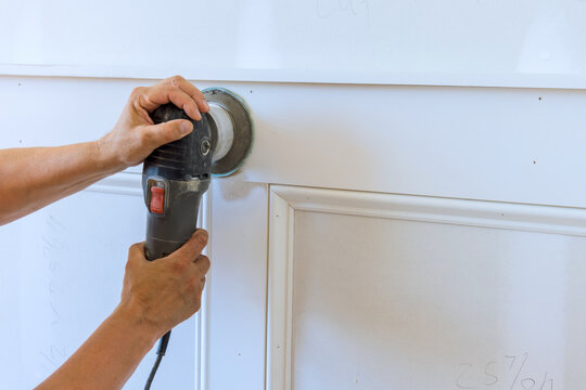 Carpenter carefully operating sander on white wood paneling during home improvement task.