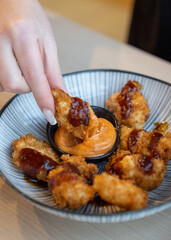 Crispy nuggets held by hand with dipping sauce.
