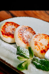 Delicious cheese pancakes with powdered sugar and mint on a rustic plate