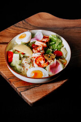 Colorful salad bowl with shrimp, eggs, and fresh vegetables served on a wooden plate