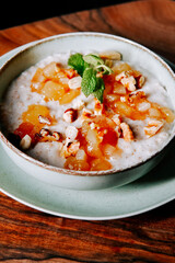 Delicious bowl of creamy oatmeal topped with fresh fruits and nuts on wooden table