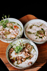Three bowls of creamy soup with seafood and green garnishes on a wooden platter