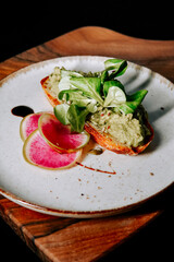 Delicious avocado toast topped with fresh greens and pickled radishes served on a wooden board