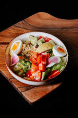 Colorful salad with fresh vegetables and boiled eggs presented on a wooden surface
