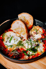 Delicious dish of eggs simmered in spicy sauce with fresh herbs and bread served in a skillet
