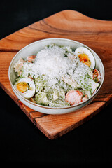 Fresh salad topped with cheese and hard-boiled eggs served on a wooden board