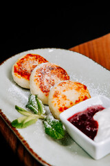 Delicious cheese pancakes served with jam and sour cream on a rustic plate