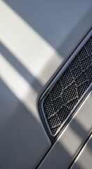 Close-up of a modern cars side vent with sunlight and shadows highlighting its intricate design and sleek lines, showcasing automotive detail and luxury.