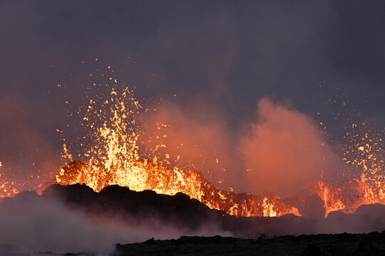 View of molten lava erupting in a volcanic display, contrasting against the dark sky with billowing smoke, in a moment of geological drama, Reykjanes, Grindav&iacute;kurbaer, Iceland.