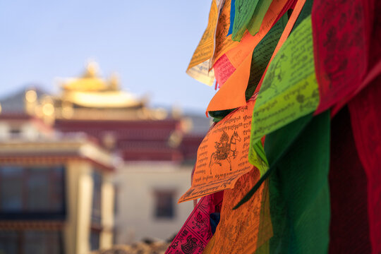 View of vibrant Tibetan prayer flags fluttering in the breeze, framing the blurred golden roof of a distant temple, Diqing Tibetan Autonomous Prefecture, Yunnan, China.
