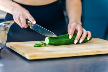 Woman slices cucumber in kitchen closeup. Fresh salad.