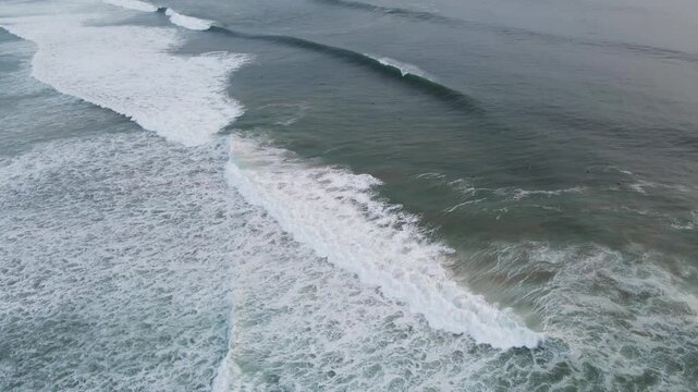 Aerial view of the powerful ocean waves rolling towards the shore, creating a dynamic interplay of dark water and foamy white crests, Costa da Caparica, Setubal, Portugal.
