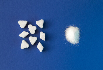 Sugar piece cubes and white crystal granulated sugar comparison on blue background. Top view closeup.