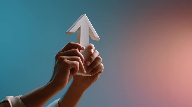 Hands holding white arrow prop pointing upward with soft gradient background symbolizing growth progress direction and positive symbol of success