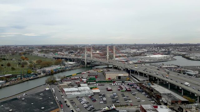 Panning drone shot across factories and NYC waterfront, revealing an expansive industrial zone with East River views and skyline silhouettes on the horizon. Dramatic urban perspective.