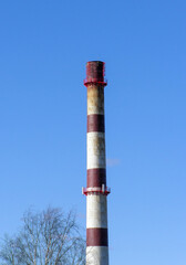 Tall boiler house chimney with red and white stripes against clear blue sky, industrial infrastructure concept.