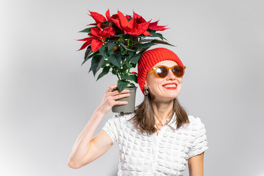 Joyful beautiful woman holding winter red flowers wearing red hat. Woman celerbrating winter with Christmas bouquet