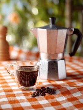 A cup of coffee and beans, coffee maker with bokeh on background