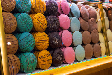 Assortment of vibrant hand-decorated gingerbread rounds in multiple colors and textures, arranged behind a glass counter with festive light reflections. Selective focus

