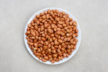 Raw, shelled peanuts piled on a white plate, ready for roasting.