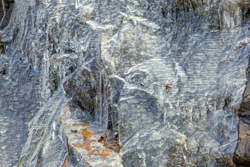 Narrow streams of water run under a thin sheet of ice and over stone