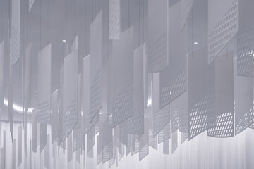 a series of geometric, lattice-patterned paper lanterns hanging from the ceiling. The lanterns are rectangular with a grid-like design, casting intricate shadows on a white, softly lit background