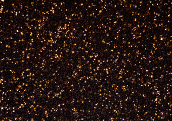 a textured surface covered in small, glittering particles. The background is dark brown, almost black, while the particles are golden-yellow, creating a sparkling effect