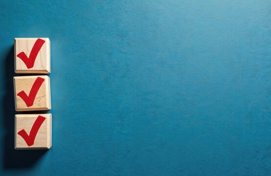 Three wooden blocks stacked vertically show red check marks. This represents confirmation, completion, and successful tasks on a blue textured surface. - Powered by Adobe